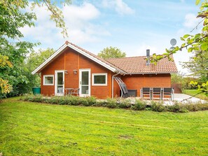 Ett trähus med ett tak täckt av takpannor, en ytterdörr och en liten uteplats med utemöbler.