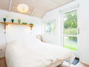 A bedroom with a bed, a wooden ceiling, a window, and a door leading to a garden.
