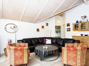 A living room with a black leather sofa, patterned armchairs, a round coffee table, and a wooden ceiling. - 5 Star Holiday Home in Allingabro (Allingåbro)