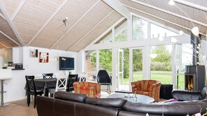 A spacious living area with a large sofa, a dining table, and chairs. There is a television mounted on the wall, and a fireplace is visible in the background. - 5 Star Holiday Home in Allingabro (Allingåbro)