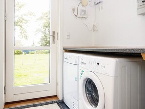 A laundry room with a front-loading washing machine, a door leading outside, and a wall-mounted electrical outlet.