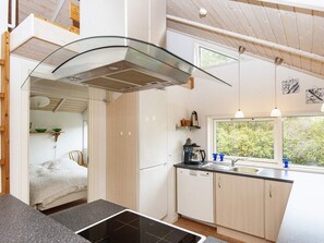 A modern kitchen with a glass cooktop, wooden cabinets, and a window overlooking greenery.