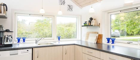 Une cuisine moderne équipée d’un lave-vaisselle, d’un évier à deux bacs et de meubles de rangement en bois.