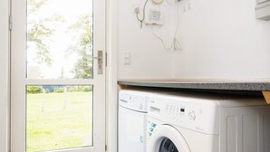 A laundry area with a front-loading washing machine, a door leading to a grassy yard, and a wall-mounted electrical outlet. - 5 Star Holiday Home in Allingabro (Allingåbro)
