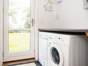 A laundry area with a front-loading washing machine, a door leading to a grassy yard, and a wall-mounted electrical outlet. - 5 Star Holiday Home in Allingabro (Allingåbro)