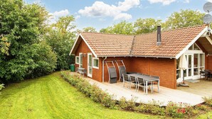 A wooden house with a tiled roof, a patio with a table and chairs, and a garden. - 5 Star Holiday Home in Allingabro (Allingåbro)