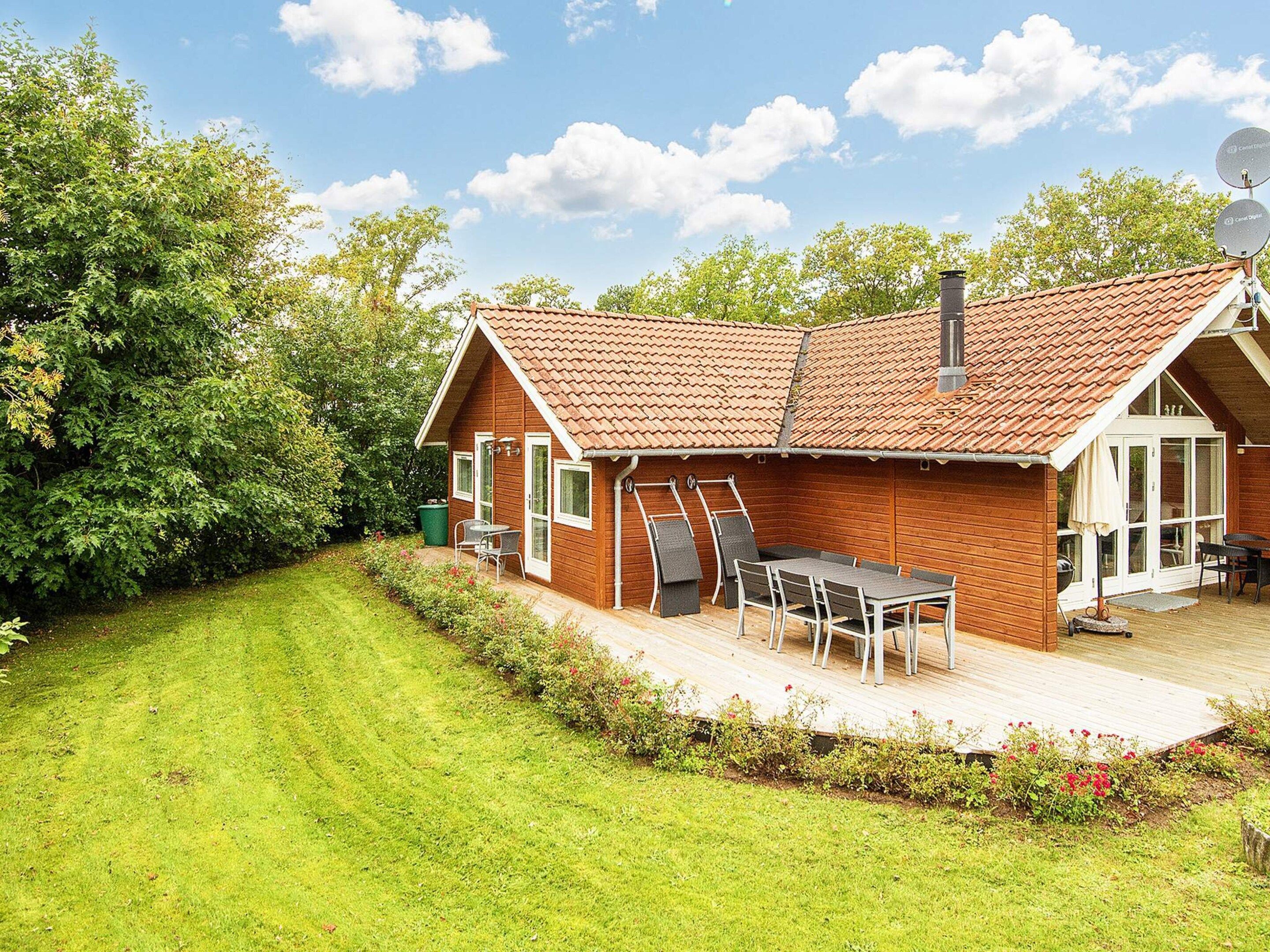 Une maison en bois avec un toit en tuiles, une terrasse avec une table et des chaises, et un jardin.