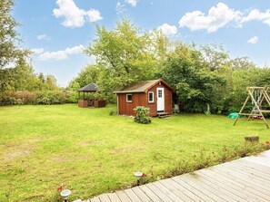 A wooden cabin with a door and window, surrounded by a grassy yard and trees. - 5 Star Holiday Home in Allingabro (Allingåbro)