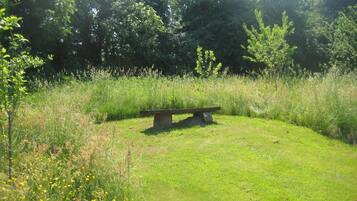 A grassy area with a stone bench surrounded by wildflowers and trees.