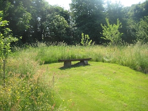 A grassy area with a stone bench surrounded by wildflowers and trees. - 6 Person Holiday Home in Hojslev (Hojslev)