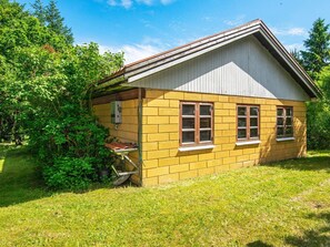 A single-story yellow building with a gabled roof, surrounded by greenery.