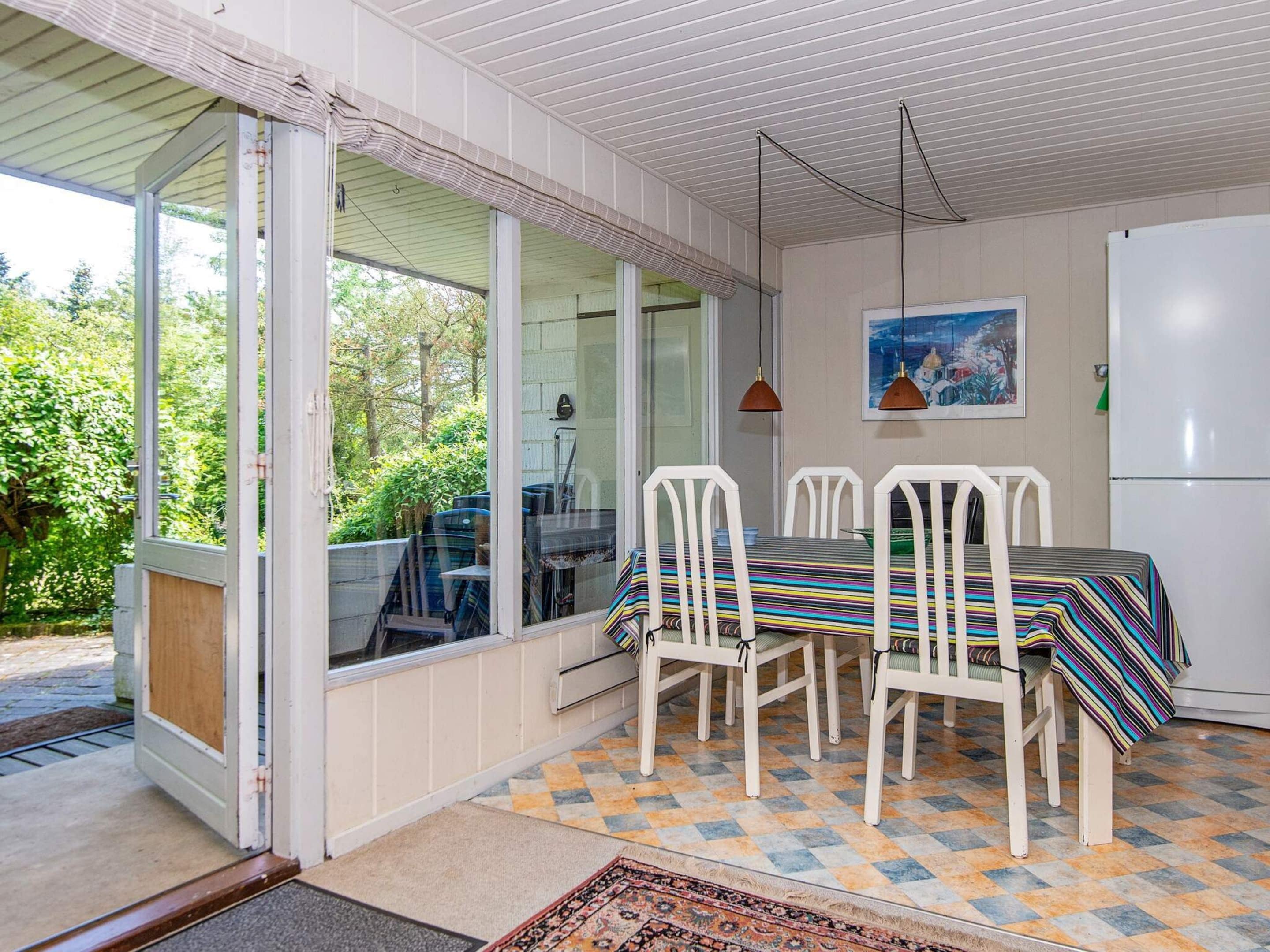 A dining area with a table and chairs, a refrigerator, and a view of greenery outside.