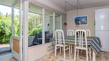 A dining area with a table and chairs, a refrigerator, and a view of greenery outside.