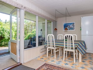 A dining area with a table and chairs, a refrigerator, and a view of greenery outside.