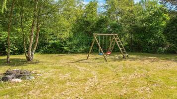 A wooden swing set in a grassy area with trees in the background.