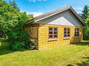 A small, single-story building with a sloped roof, surrounded by lush greenery. - 6 Person Holiday Home in Hojslev (Hojslev)