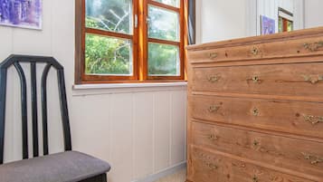Una habitación con ventana, un aparador de madera con tiradores de latón y una silla.