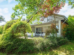 A modern house with a covered porch, surrounded by lush greenery and trees.