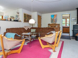 A living room with a brown sofa, a glass coffee table, and wooden chairs. There is a painting on the wall and a lamp hanging from the ceiling. - 6 Person Holiday Home in Hojslev (Hojslev)