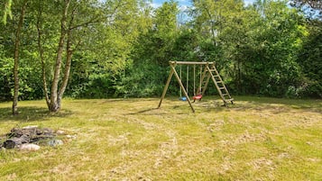 A wooden swing set in a grassy area with trees in the background.