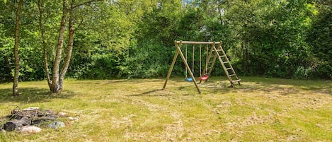 A wooden swing set in a grassy area with trees in the background.
