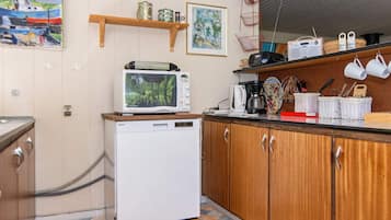 Una cocina compacta con microondas, cafetera y un refrigerador pequeño. Cuenta con armarios de madera y piso de baldosas.