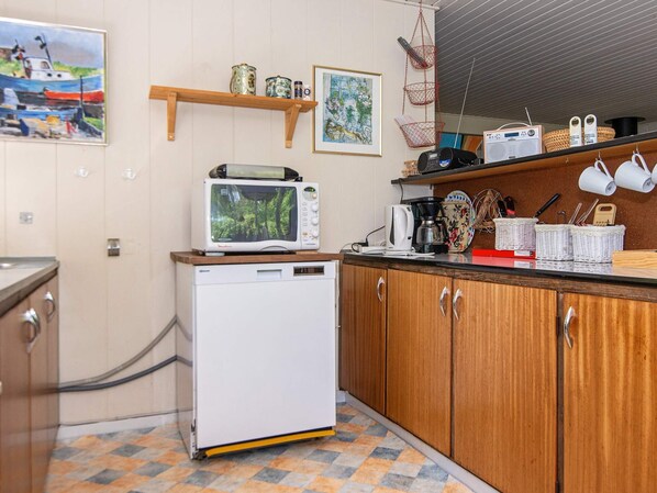 A compact kitchen with a microwave, coffee maker, and a small refrigerator. There are wooden cabinets and a tiled floor. - 6 Person Holiday Home in Hojslev (Hojslev)