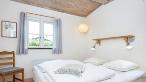 A bedroom with a bed, a chair, a window with curtains, and a wall-mounted light fixture. - Renovated Cottage Near Beach - By Traum Ferienwohnungen (Borkop)