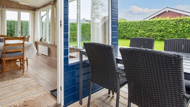 A covered patio area with a table and chairs, a view of a garden, and a red barn in the background. - Renovated Cottage Near Beach - By Traum Ferienwohnungen (Borkop)