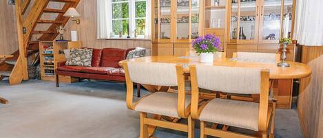 A cozy interior with a wooden dining table, cushioned chairs, a red sofa, and a staircase.