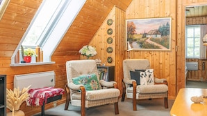 A cozy room with wooden walls, a sloped ceiling, a dining table, two armchairs, a bookshelf, and a painting. - 6 Person Holiday Home in Hals (Hals)