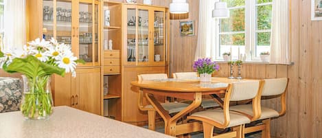 A wooden-paneled room with a dining table and chairs, a cabinet with glass doors, and a window with curtains.