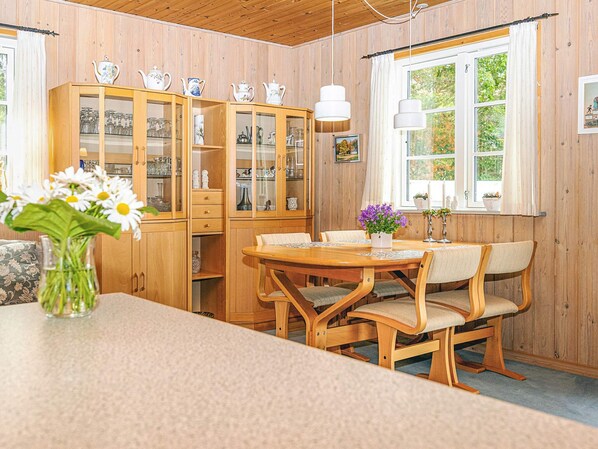 A wooden-paneled room with a dining table and chairs, a cabinet with glass doors, and a window with curtains.