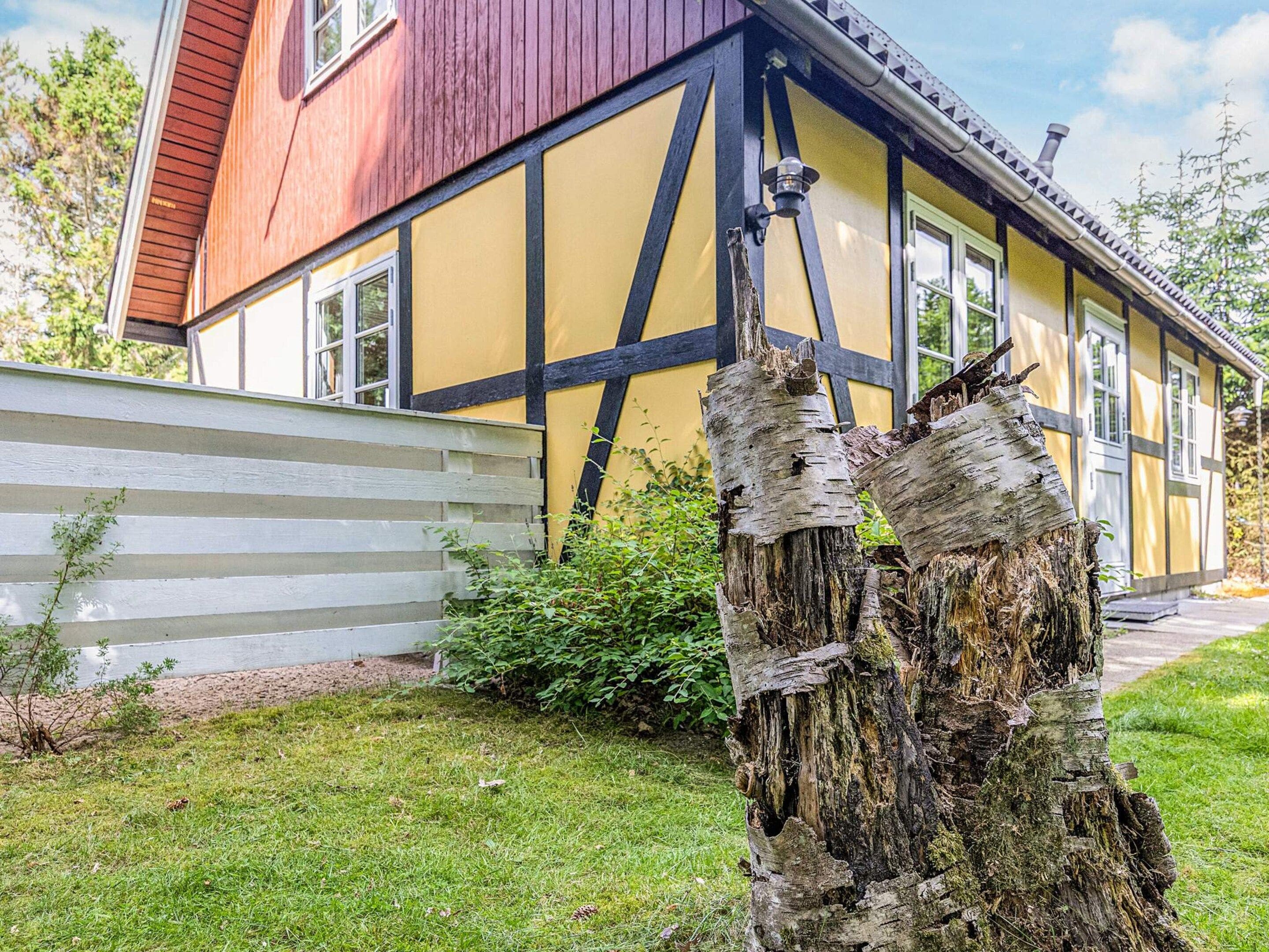 A traditional half-timbered house with a white fence and a tree stump in the foreground.