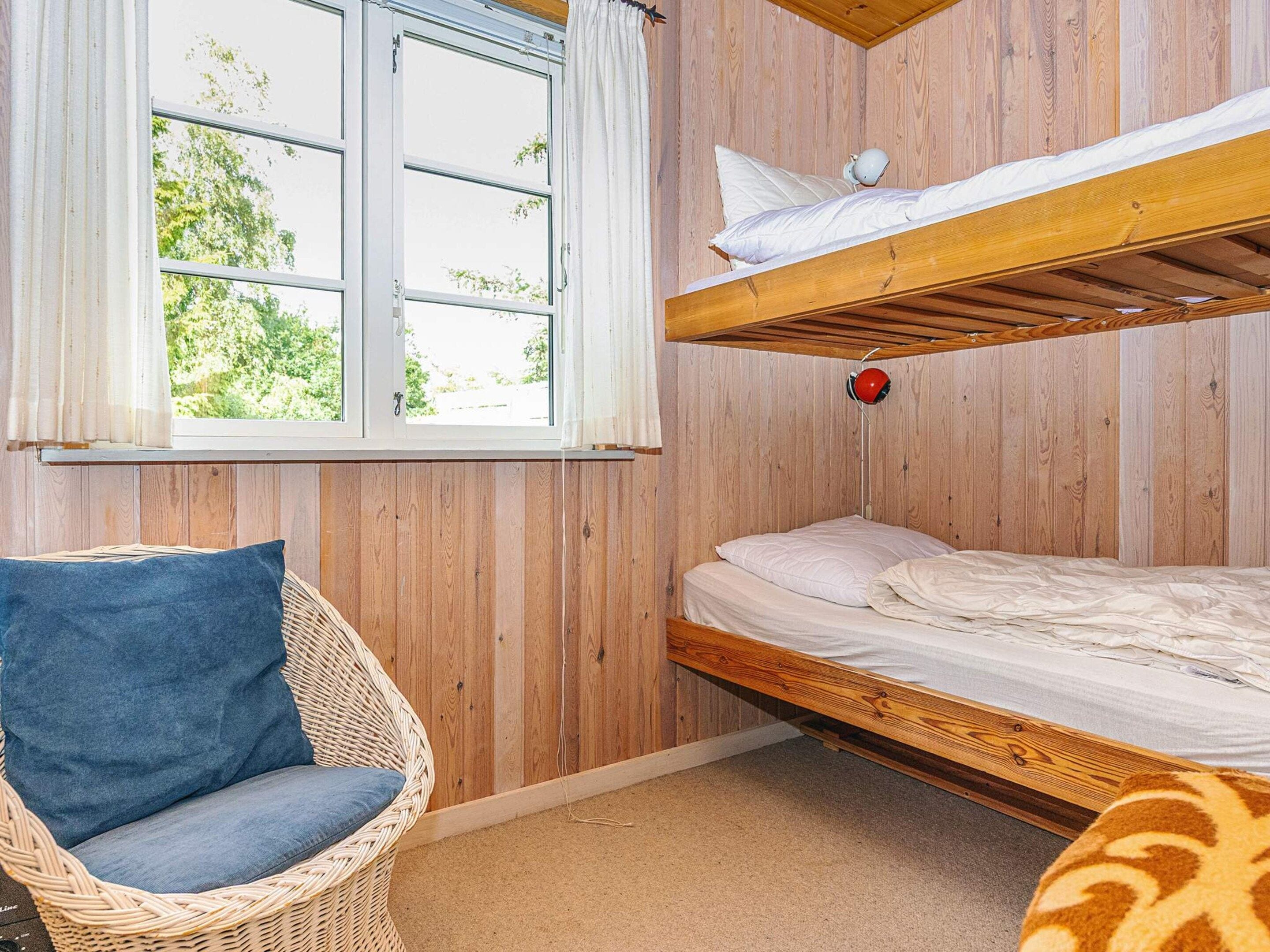 A room with a bunk bed, a wicker chair, and a window with curtains.