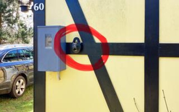 Una pared amarilla con un candado negro y rojo, un coche azul al fondo y un cartel con el número 60.