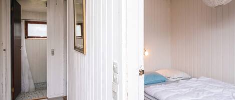 Een slaapkamer met een bed, een hanglamp en een deur naar een andere kamer.