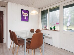 A dining area with a glass table and brown chairs, a pendant light, a window with plants, and a purple artwork.