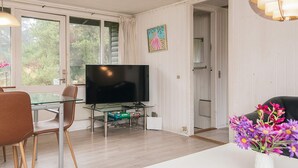Moderni olohuone, jossa on litteänäyttöinen televisio, lasinen ruokapöytä ja tuolit.