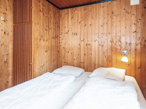 Una habitación con paredes de paneles de madera, una cama con ropa blanca y una lámpara fijada a la pared.