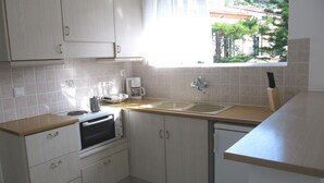 Una cocina con microondas, cafetera y lavamanos. Se ve una ventana con vistas a árboles y edificios.