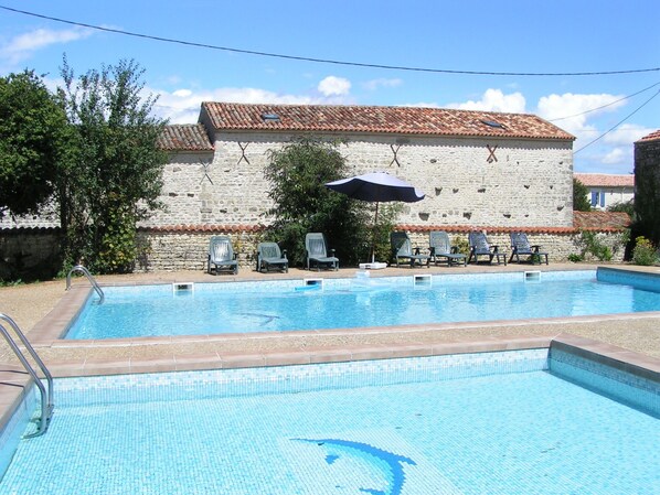 A swimming pool with lounge chairs and umbrellas, surrounded by stone buildings with tiled roofs.