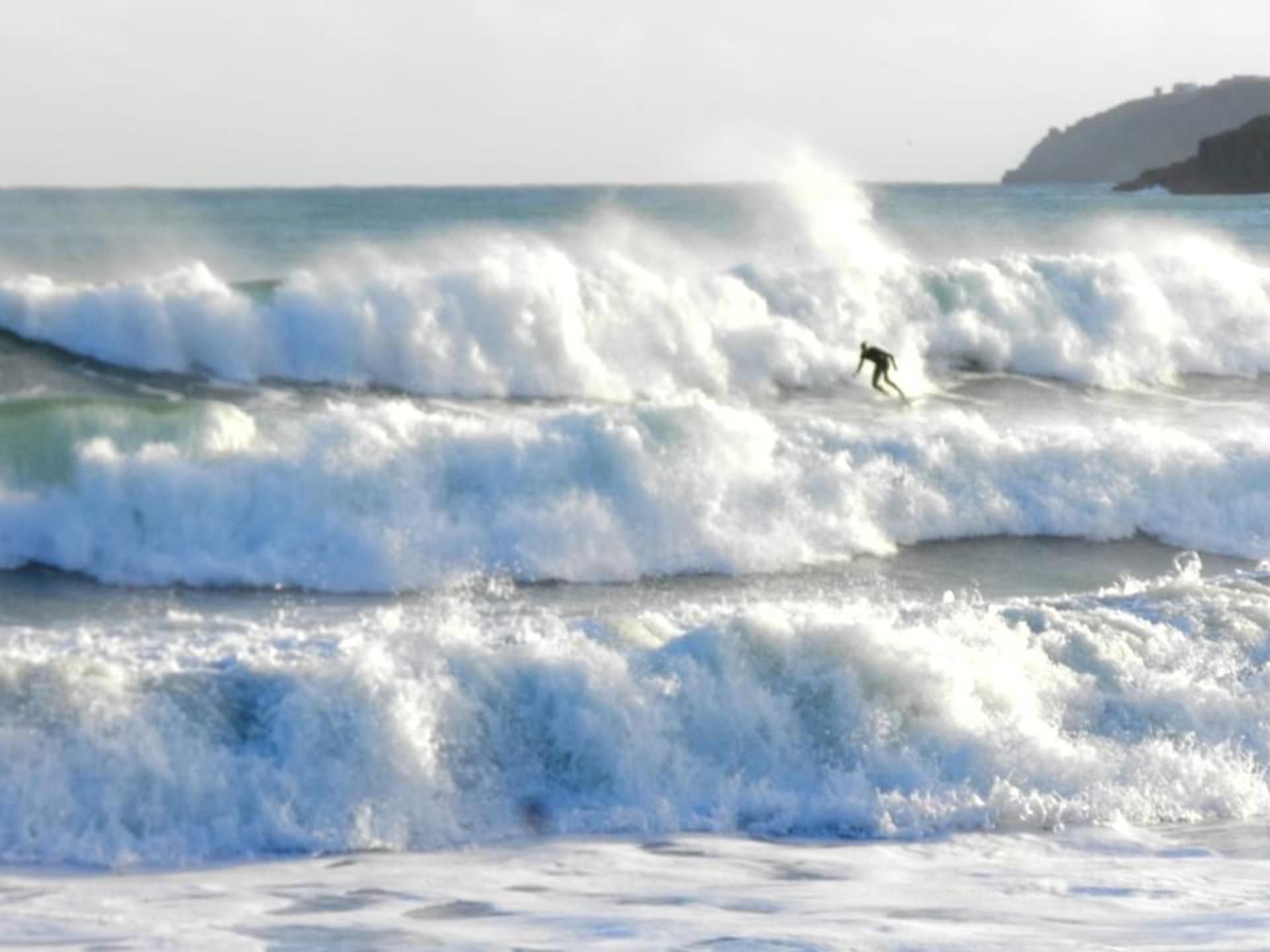 A surfer riding a wave with a mountainous coastline in the background.