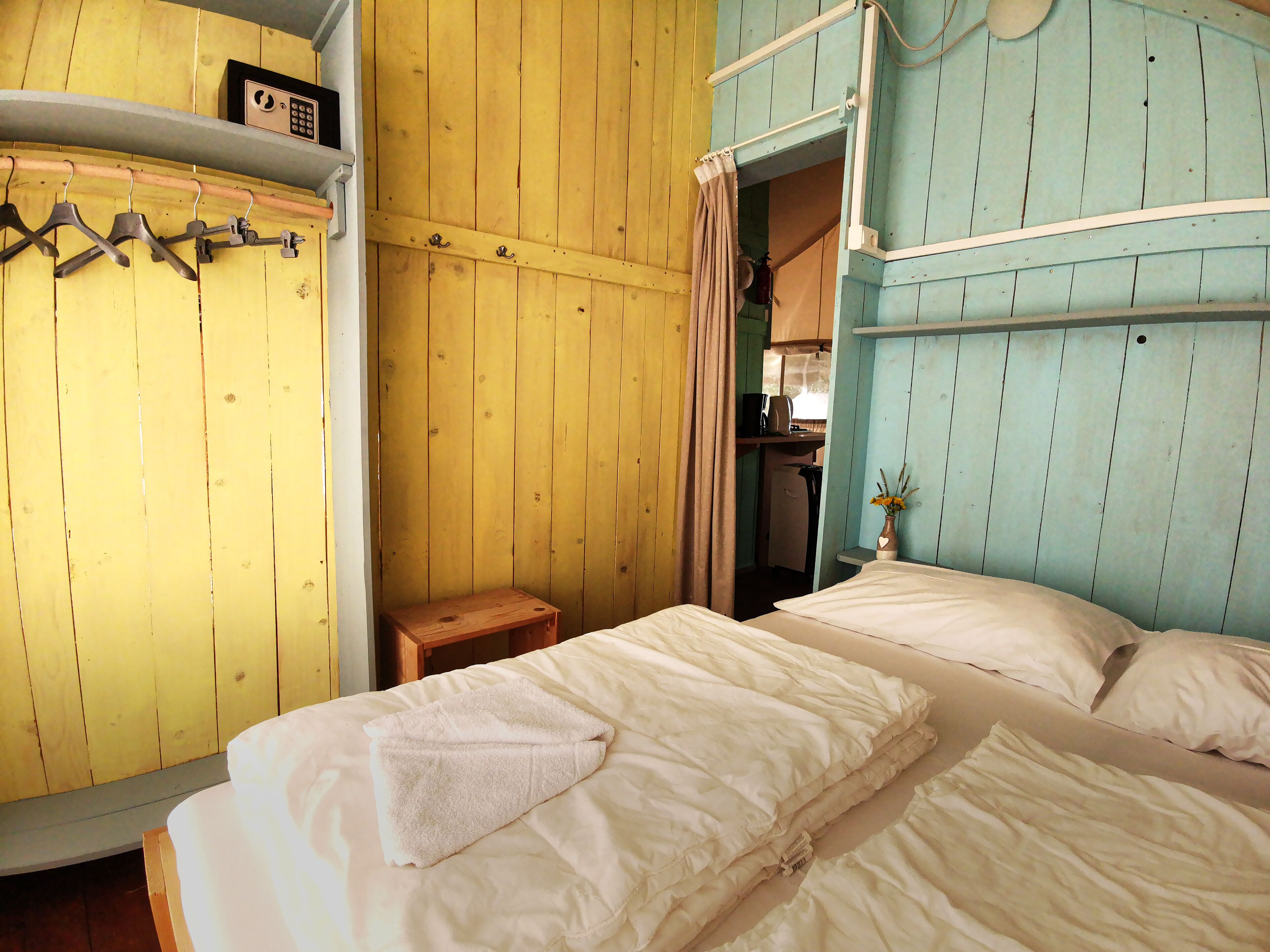 A room with a bed, a small wooden table, and a shelf with a radio.