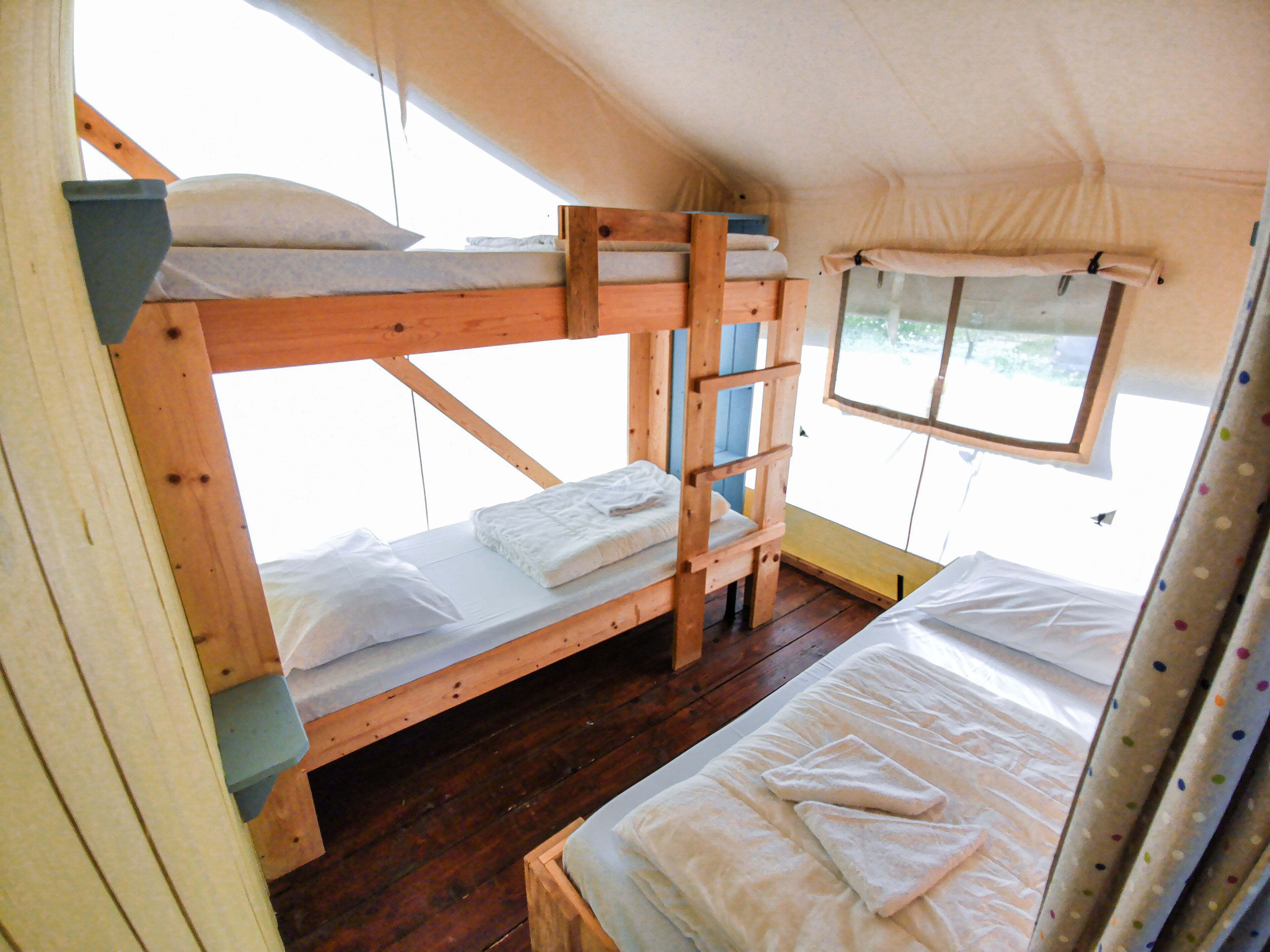 Dormitorio con literas de madera, ropa de cama blanca y ventana con vistas.