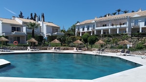 A swimming pool with lounge chairs and umbrellas, surrounded by multi-story buildings with balconies.