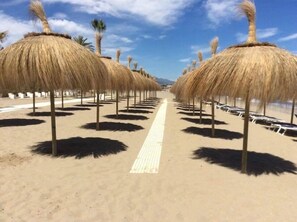 A beach with rows of thatched umbrellas and sun loungers. - Luxury,fenced townhouse, large garden, golf, ideal for home working (Benahavís)