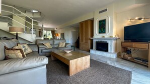 A modern living room with a sofa, coffee table, fireplace, television, and staircase.