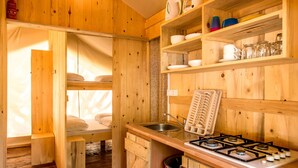 A compact wooden cabin with a bunk bed, a kitchenette with a gas stove, and shelves with dishes and glasses. - Sunflower Camping Savudrija (Umag)