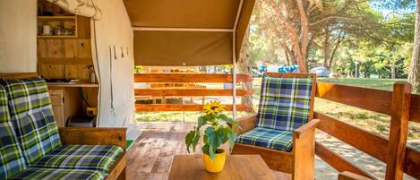 Una terraza de madera con un banco y una mesa, una planta en maceta amarilla y un banco de madera con cojines a cuadros.
